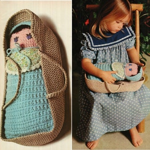 May include: A crocheted baby doll in a brown crocheted bassinet. The doll is wearing a blue and white dress and a floral print bonnet. The bassinet has a handle on each side.