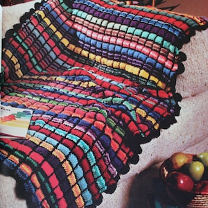 May include: A colorful crocheted throw blanket with a black border and a scalloped edge. The blanket is made with a variety of colors, including red, blue, green, yellow, and purple.