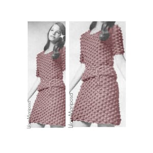 May include: A pink crochet dress with a matching top. The dress has a fitted bodice and a slightly flared skirt. The top has short sleeves and a round neckline. The dress is made with a textured stitch that creates a raised pattern.