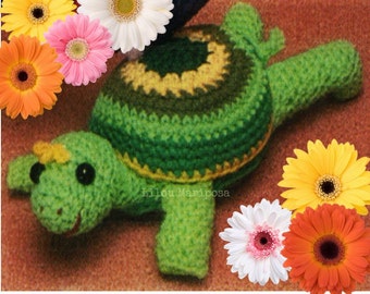 May include: A crocheted green turtle toy with a yellow nose and black eyes. The turtle's shell is green, yellow, and brown. The toy is surrounded by colorful flowers.