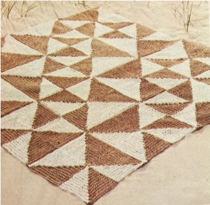 May include: A knitted blanket with a geometric pattern of alternating brown and cream-colored triangles. The blanket is square-shaped and appears to be made of a textured yarn. The design creates a visually appealing, symmetrical pattern.