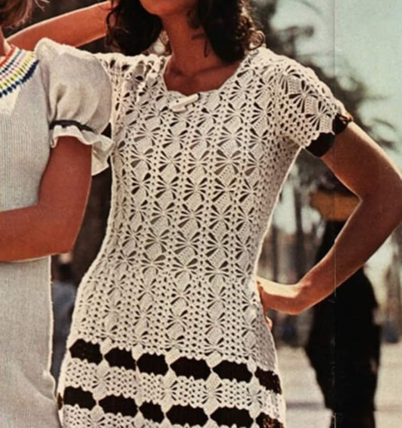 May include: A white crochet dress with a brown and white striped bottom. The dress has a round neckline and short sleeves.