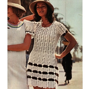 May include: A white crochet dress with brown trim. The dress has a round neckline and short sleeves. The model is wearing a wide-brimmed hat.