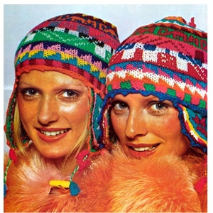 May include: Two women wearing colorful crocheted hats with ear flaps. The hats have a geometric pattern with bright colors like red, green, blue, and yellow.