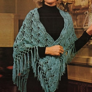 May include: A teal crochet shawl with fringe. The shawl is draped over a person's shoulders and is made with a delicate openwork pattern.