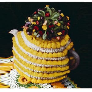 May include: A crocheted teapot cozy in yellow and white with a flower-shaped top made of colorful yarn.