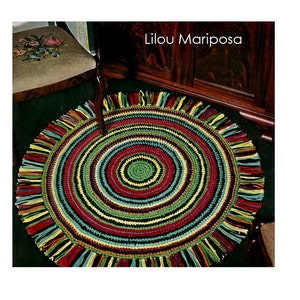 May include: A colorful round crochet rug with a fringe border. The rug has a multi-colored striped pattern with a smaller green circle in the center. The rug is called "Lilou Mariposa".