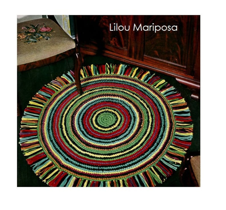 May include: A colorful round crochet rug with a fringe border. The rug has a multi-colored striped pattern with a smaller green circle in the center. The rug is called "Lilou Mariposa".