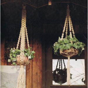 Puede incluir: Dos maceteros de macramé con plantas verdes colgando de un porche de madera. Los maceteros están hechos de cuerda natural y tienen un borla en la parte inferior. El texto "Interessante" y "Au Naturel" es visible en el porche.