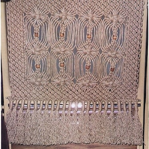 May include: A macrame wall hanging with a geometric pattern and wooden beads. The hanging has a fringe at the bottom.