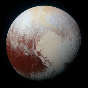 May include: A close-up view of Pluto, a dwarf planet in the Kuiper Belt. The surface is a mix of reddish-brown and light gray, with hints of blue. The planet is round and appears to be covered in craters and other geological features.