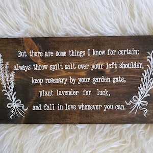 May include: A rustic wooden sign with white text that reads: "But there are some things I know for certain: always throw spilt salt over your left shoulder, keep rosemary by your garden gate, plant lavender for luck, and fall in love whenever you can."