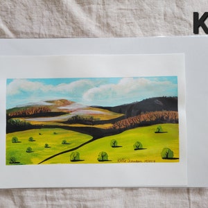 May include: A watercolor painting of a landscape with rolling hills, a blue sky with white clouds, and green trees. The painting is signed "Kellie Cranbrook 2018".