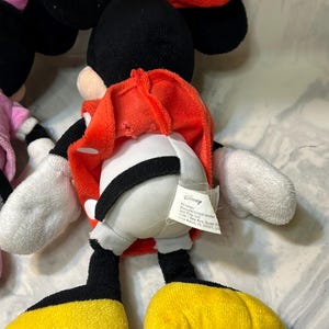 May include: A plush Minnie Mouse doll with a red bow, black ears, and a red dress. The doll has white gloves, black legs, and yellow shoes. A Disney tag is attached.
