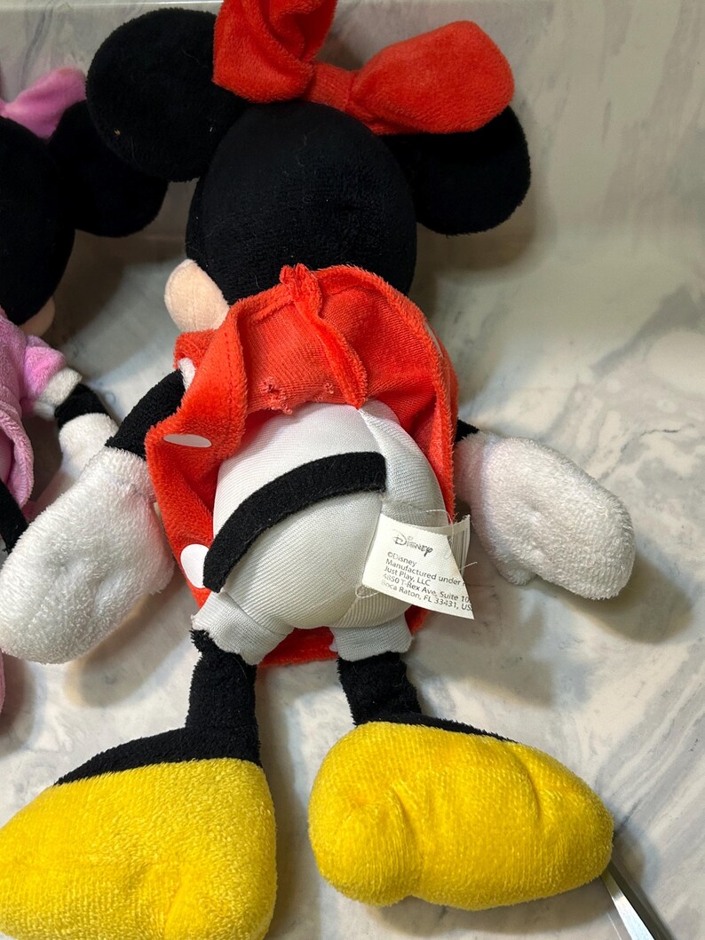 May include: A plush Minnie Mouse doll with a red bow, black ears, and a red dress. The doll has white gloves, black legs, and yellow shoes. A Disney tag is attached.