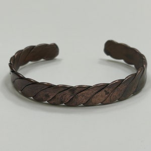 May include: A braided copper bracelet with a dark brown finish.