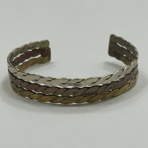 May include: A braided cuff bracelet made of three different metals: silver, copper, and brass.