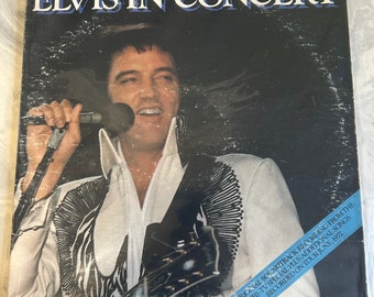 May include: A black and white vinyl record album cover featuring Elvis Presley singing into a microphone. The album cover is titled "Elvis in Concert" and includes the text "Original Soundtrack Recording from the CBS-TV Special Plus Additional Songs Recorded on Tour June, 1977."