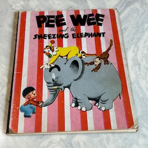 May include: Vintage children's book titled "Pee Wee and the Sneezing Elephant." The cover features a cartoon illustration of a gray elephant, a clown, a monkey, and a small boy. The background has pink and red vertical stripes.