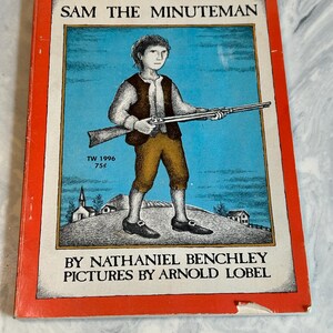 May include: A vintage children's book titled "Sam the Minuteman" with a colorful illustration of a young boy holding a rifle. The cover features a red border and the author and illustrator's names. The book is from 1996.
