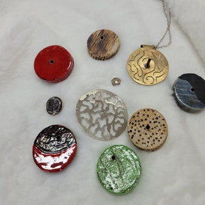 May include: Assortment of round ceramic and metal pendants with various patterns and colors, including red, green, black, white, and brown. Some pendants have a hole in the center.
