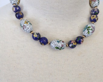 May include: A white and blue cloisonné necklace with floral designs. The necklace is made of oval-shaped beads with gold accents.