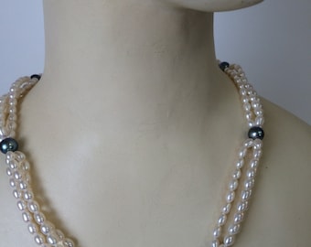 Puede incluir: Un collar de perlas de tres hileras con perlas blancas y cuatro perlas negras como detalles.