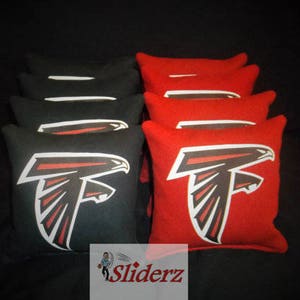 May include: A stack of red and black bean bags with a football team logo. The logo is a black and red falcon with the words "Sliderz" printed on the bottom.