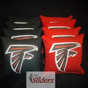 May include: A set of bean bags with a black and red color scheme. The bean bags feature a white graphic of a falcon with a red and black design. The bean bags are arranged in a stack with the red bean bags on top and the black bean bags on the bottom.