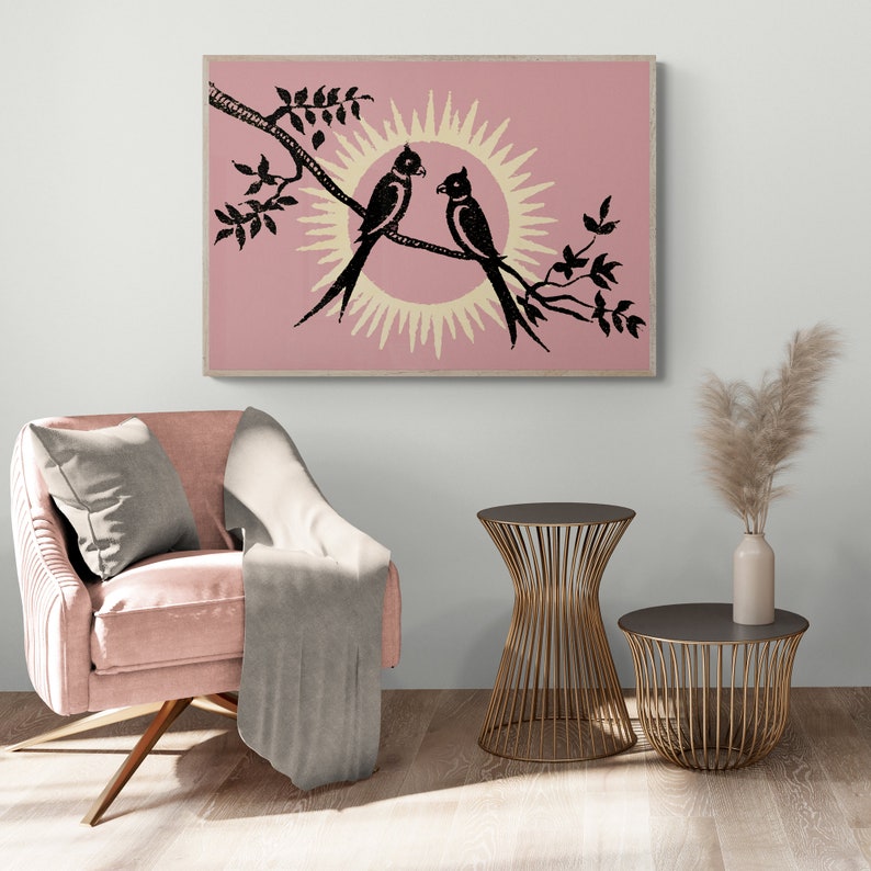 K&ouml;nnte beinhalten: Ein rosa-wei&szlig;er Druck von zwei schwarzen V&ouml;geln, die auf einem Ast sitzen, mit einer Sonne dahinter. Der Druck ist gerahmt und h&auml;ngt an einer Wand.