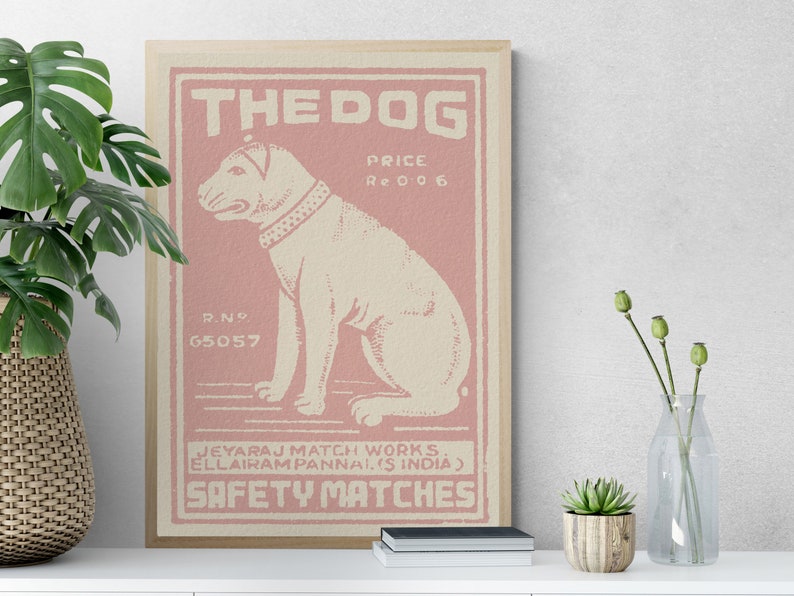 May include: A vintage-style illustration of a dog on a pink background. The illustration is framed and has the text "THE DOG", "PRICE Re 006", "R.N 65057", "JEYARAJ MATCH WORKS. ELLAIRAM PANNAI.IS INDIA)", and "SAFETY MATCHES".