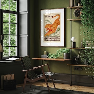 May include: A vintage poster with a tiger illustration and the text "TAMCO THE ANGAMALE MATCH CO. LTD. ANGAMALI, S.I. SAFETY MATCHES". The poster is framed and hanging on a green wall in a home office.