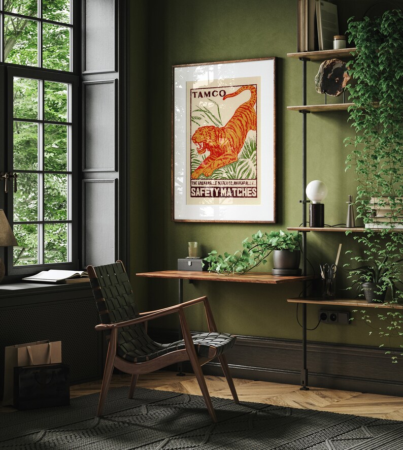 May include: A vintage poster with a tiger illustration and the text "TAMCO THE ANGAMALE MATCH CO. LTD. ANGAMALI, S.I. SAFETY MATCHES". The poster is framed and hanging on a green wall in a home office.