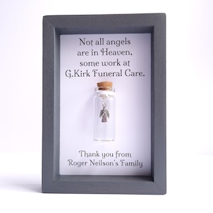 May include: A framed message with a small glass bottle containing a silver angel charm. The message reads "Not all angels are in Heaven, some work at G.Kirk Funeral Care." and "Thank you from Roger Neilson's Family."
