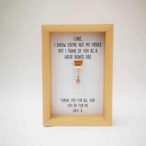 May include: A framed message in a wooden frame with a small glass bottle containing a star charm. The message reads "Chris, I know you're not my father but I think of you as a great bonus dad. Thank you for all that you do for me. Lucy X."