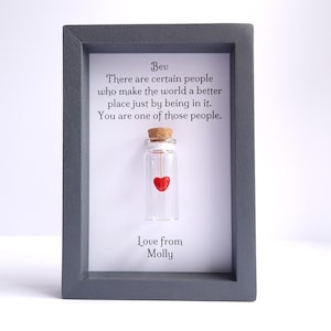 May include: A framed message with a small glass bottle containing a red heart. The message reads "Bev There are certain people who make the world a better place just by being in it. You are one of those people. Love from Molly."