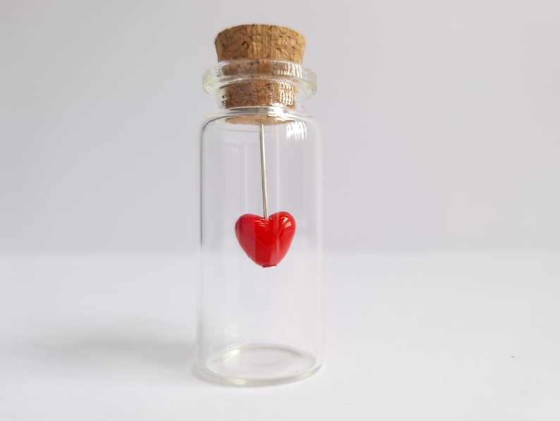 A small glass bottle with a cork stopper containing a red heart-shaped object.