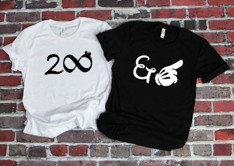 Puede incluir: Dos camisetas de manga corta, una blanca y otra negra, se muestran contra una pared de ladrillos. La camiseta blanca tiene un s&iacute;mbolo de infinito negro con el n&uacute;mero 2 a la izquierda. La camiseta negra tiene las letras "E &" con una mano blanca que apunta hacia la derecha.