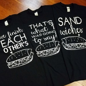 Op de afbeelding: Drie zwarte t-shirts met witte tekst en sandwich illustraties. E&eacute;n shirt leest "we finish EACH OTHER'S", een ander zegt "THAT'S what I WAS GOING to say!", en de derde zegt "SAND wiches".