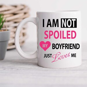 May include: White ceramic mug with a black and pink design. The mug reads "I am not spoiled my boyfriend just loves me" with a pink heart.