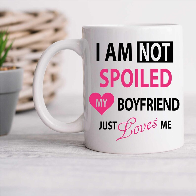May include: White ceramic mug with a black and pink design. The mug reads "I am not spoiled my boyfriend just loves me" with a pink heart.