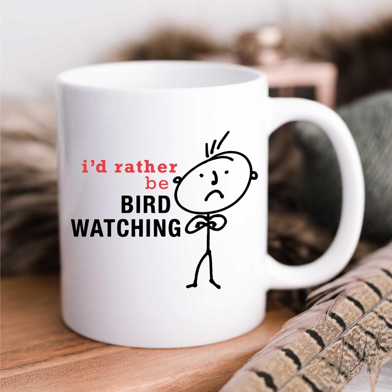 May include: White ceramic mug with a black and white illustration of a stick figure with a sad face. The text "i'd rather be BIRD WATCHING" is printed on the mug.