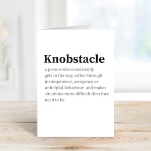 May include: A white card with the word "Knobstacle" in bold black lettering. The card defines "Knobstacle" as someone who consistently obstructs, making situations more difficult.
