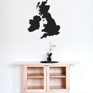 Peut inclure: Une silhouette noire du Royaume-Uni et de l'Irlande sur un mur blanc au-dessus d'une armoire en bois clair avec des portes en verre.