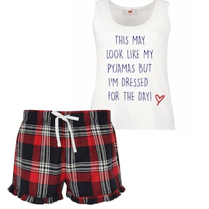 May include: White tank top with the text "This may look like my pajamas but I'm dressed for the day!" in blue with a red heart. Red and black plaid pajama shorts with a white drawstring.