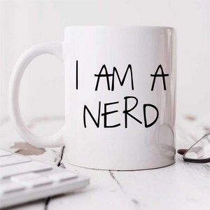 May include: White ceramic coffee mug with a black handwritten inscription that reads "I AM A NERD".