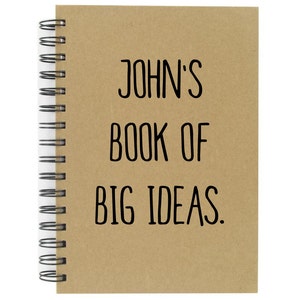 May include: A brown spiral bound notebook with the text "JOHN'S BOOK OF BIG IDEAS." printed on the cover.