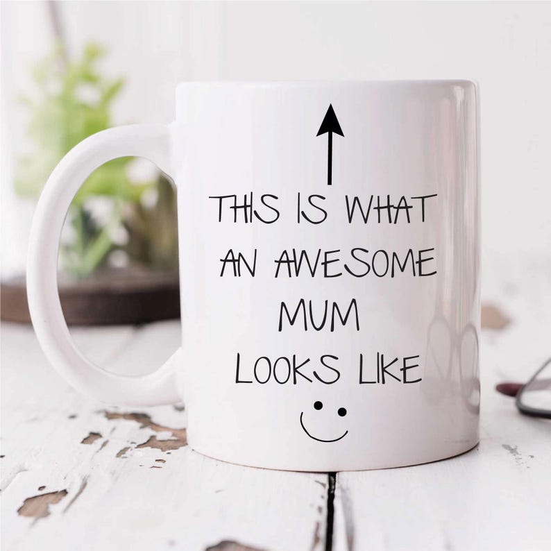 May include: White ceramic coffee mug with a black arrow pointing up and the text "This is what an awesome mum looks like" with a smiley face underneath.