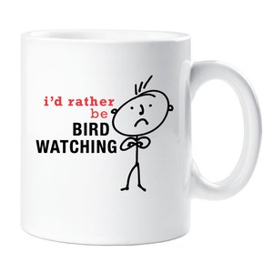 May include: White ceramic coffee mug with a black and white stick figure illustration of a person with a sad face. The text on the mug reads "i'd rather be BIRD WATCHING".