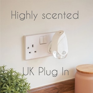 May include: A white plug-in air freshener with a clear, round diffuser. The air freshener is plugged into a UK standard electrical outlet. The text "Highly scented" is written above the air freshener and "UK Plug In" is written below the air freshener.